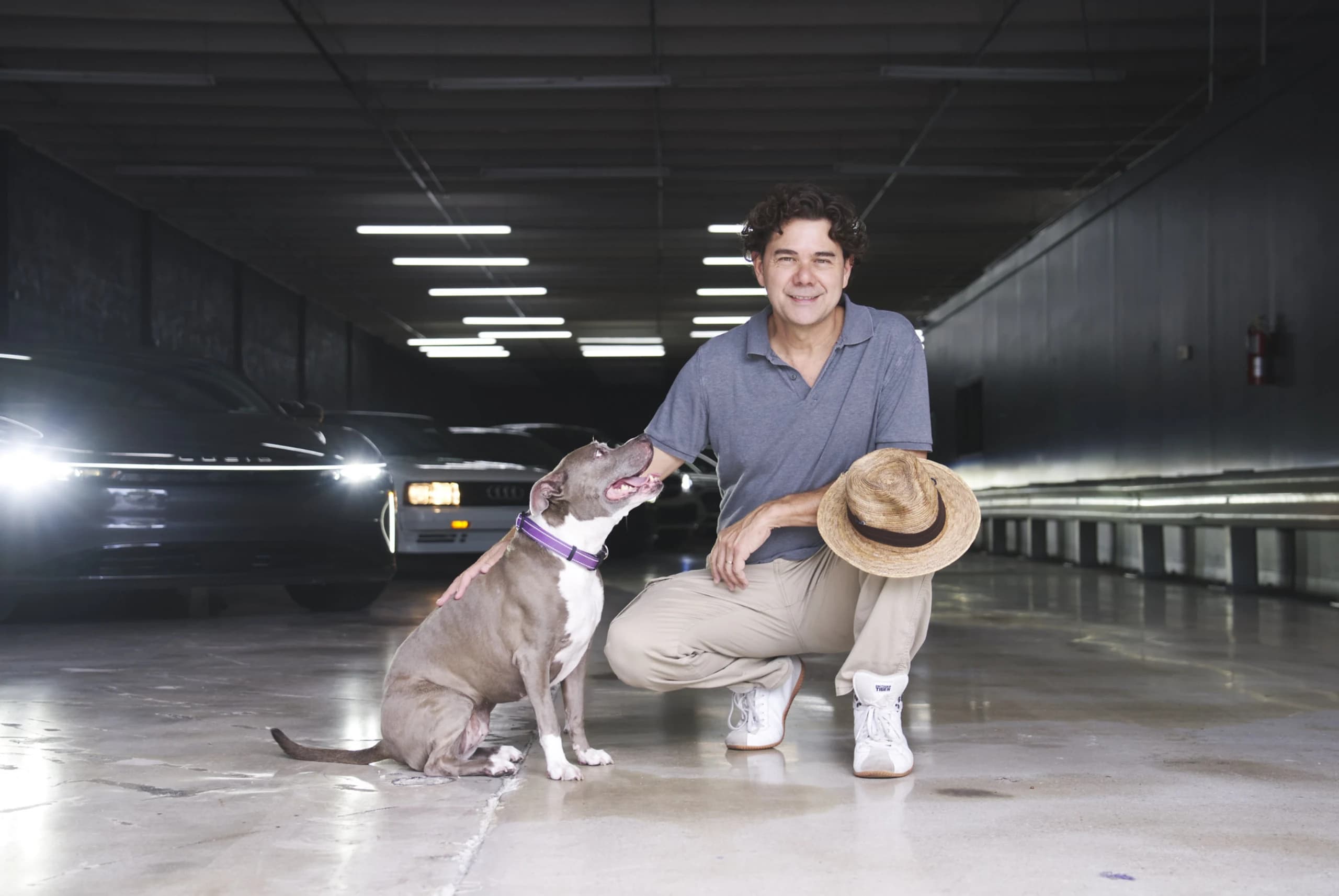 Founder Ken Russell crouching beside his dog on the storage floor at Full Stop Garage, with stored cars behind them