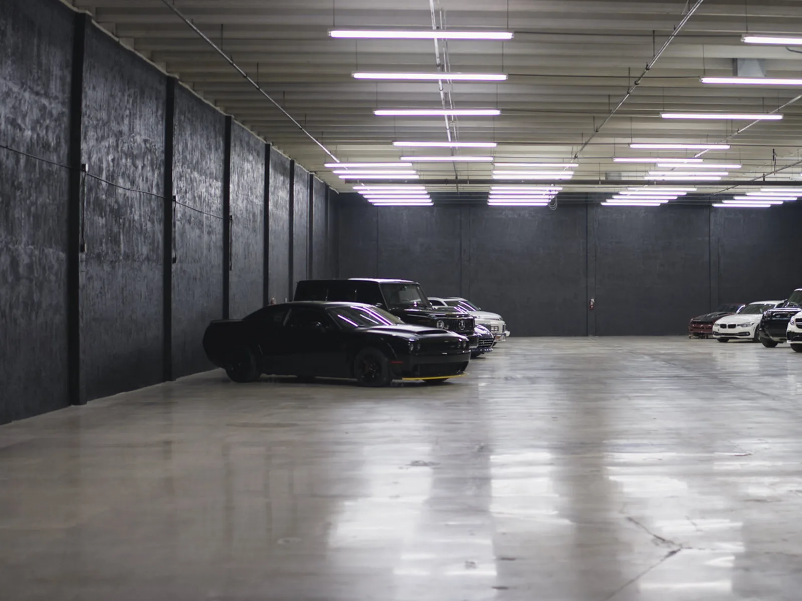 The storage floor, lit end to end, with cars parked along the left wall