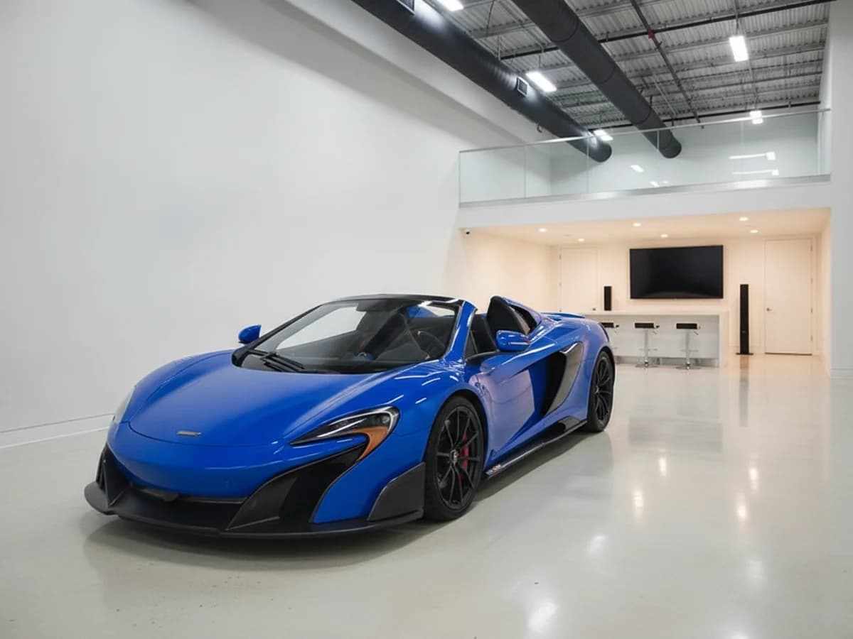 A blue McLaren 675LT alone in a private car condo bay, a loft mezzanine and a small lounge behind it on a mirror-polished floor