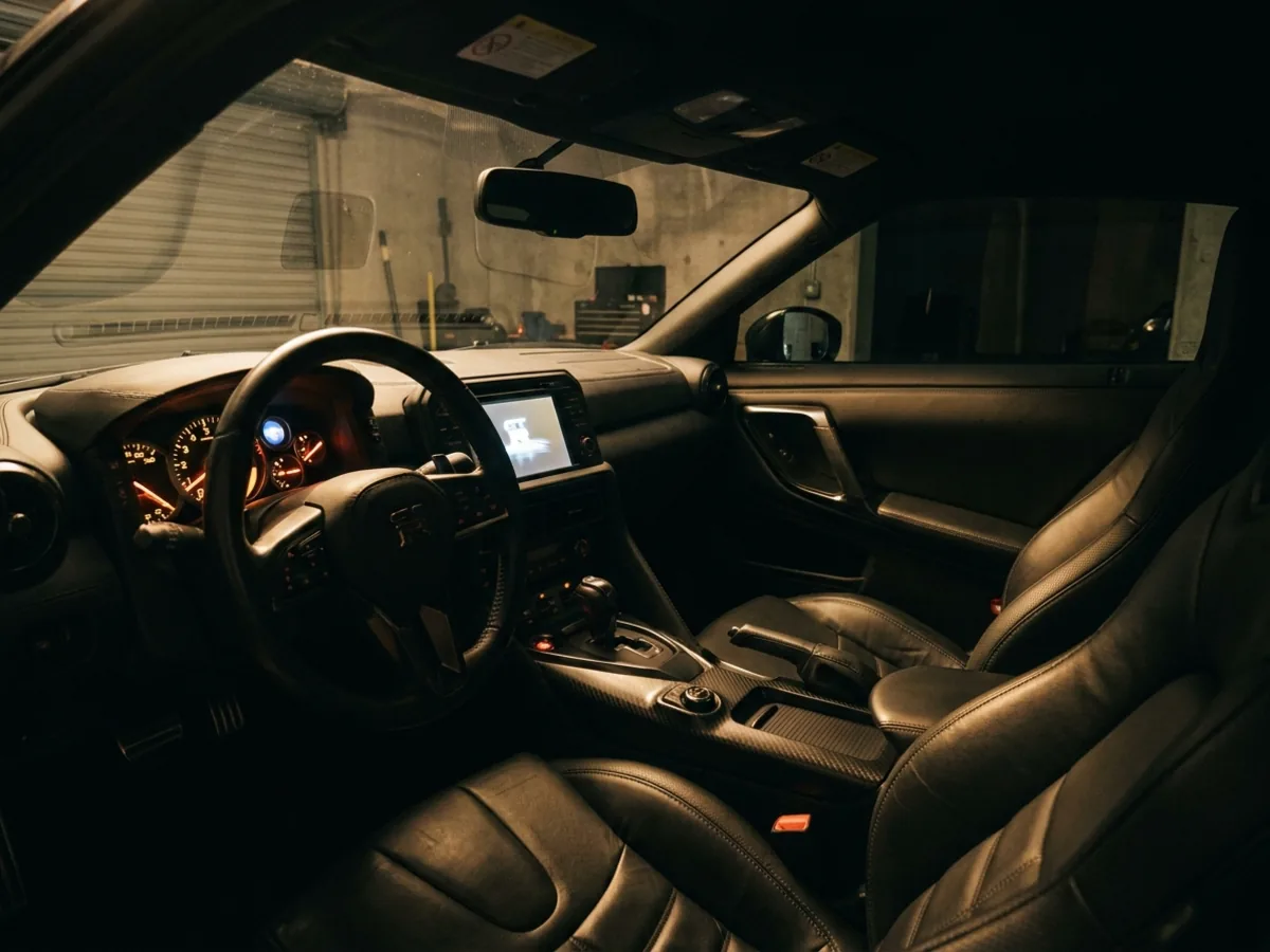 The lit cockpit of a performance car at start-up, instruments glowing and the start button burning amber, a dim garage beyond the windscreen