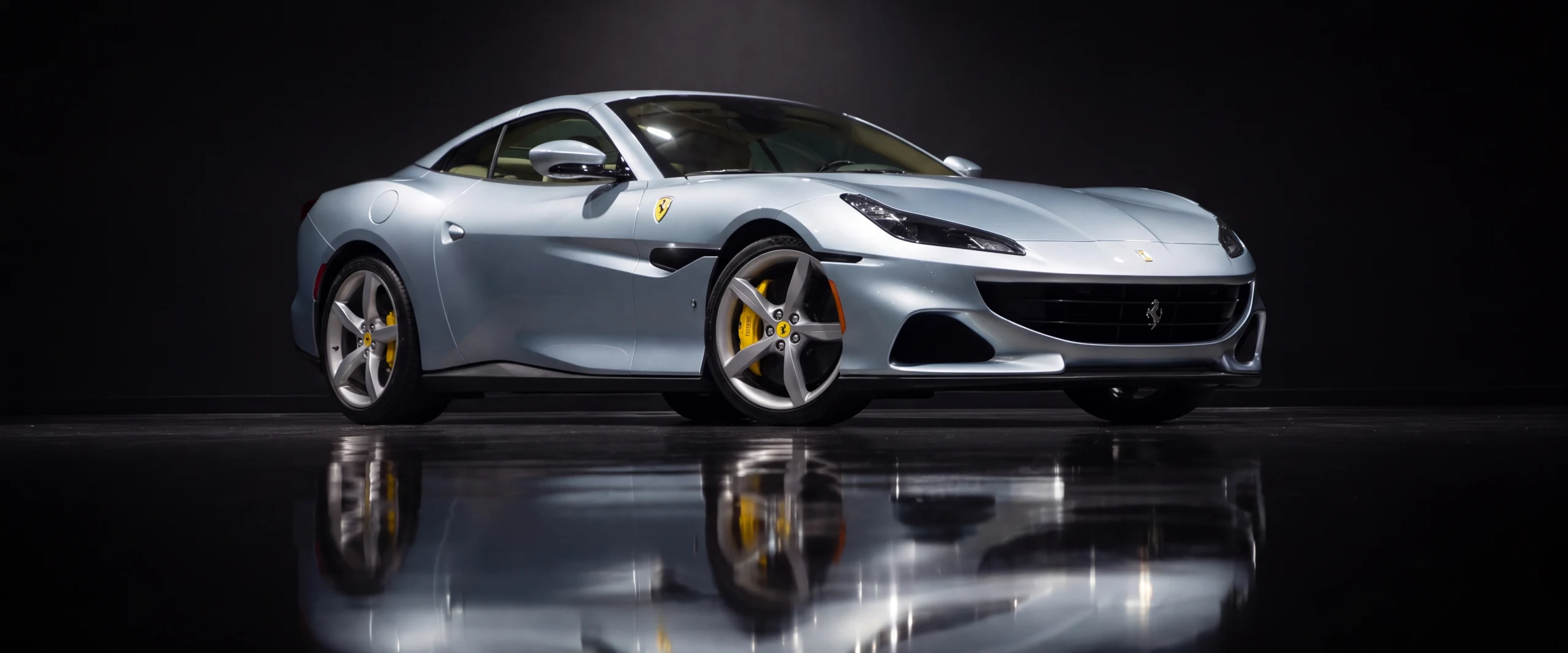A silver-blue Ferrari Portofino lit like a museum exhibit on a mirror-black floor
