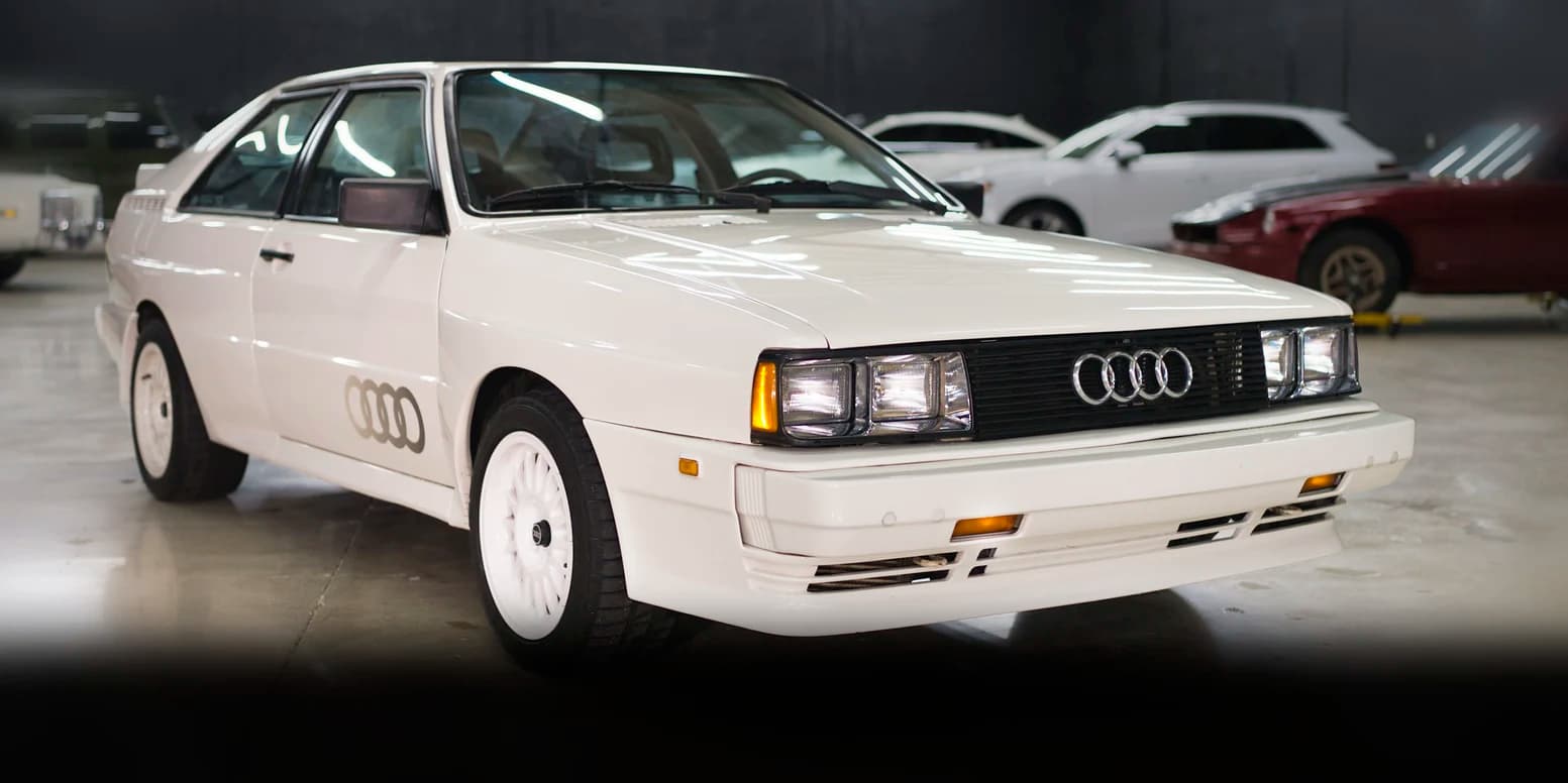 A white Audi Quattro parked on the floor at Full Stop Garage, with stored cars along the wall behind it