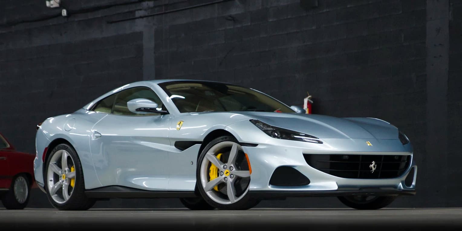 A silver Ferrari Portofino on a dark garage floor, photographed against a grey block wall