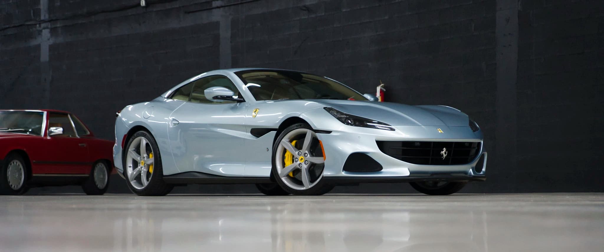 A silver Ferrari Portofino parked against a grey block wall on the storage floor