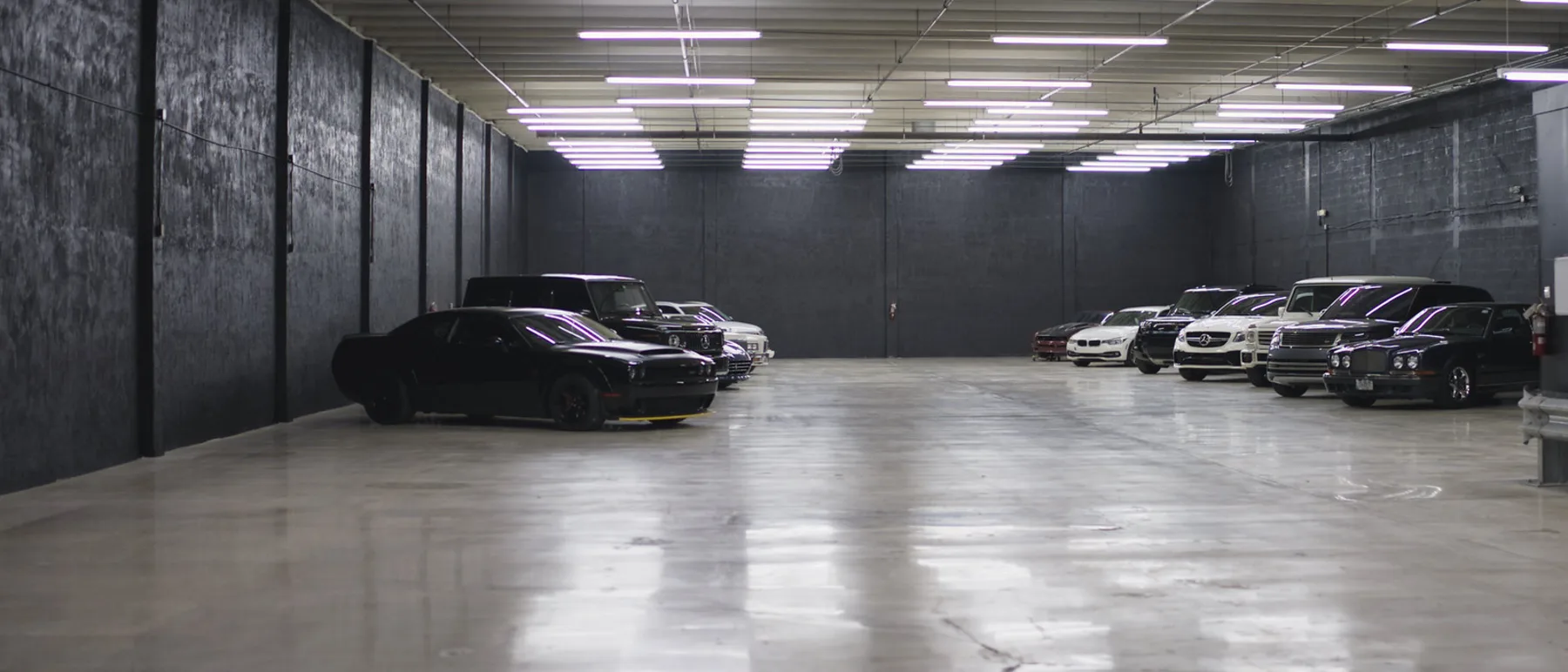 The storage floor, lit end to end, with cars parked along the wall